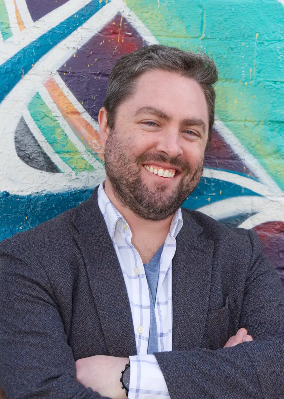 Smiling man in casual business attire with colorful graffiti background.